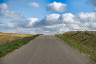 Güneşli bir günde, mavi gökyüzü ve dağınık bulutlarla ufka doğru uzanan boş kırsal yol.