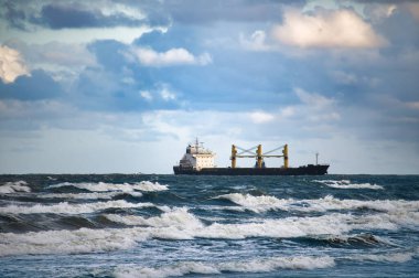 Kargo gemisi çalkantılı okyanus dalgalarında yol alıyor. Arkaplandaki bulutlara karşı. Deniz taşımacılığını ve macerayı yakalıyor..