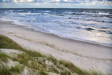 Kıyı sahnesinde kumlu bir sahilde parçalı bulutlu bir gökyüzünün altında, huzur ve huzur veren bir ortam var..