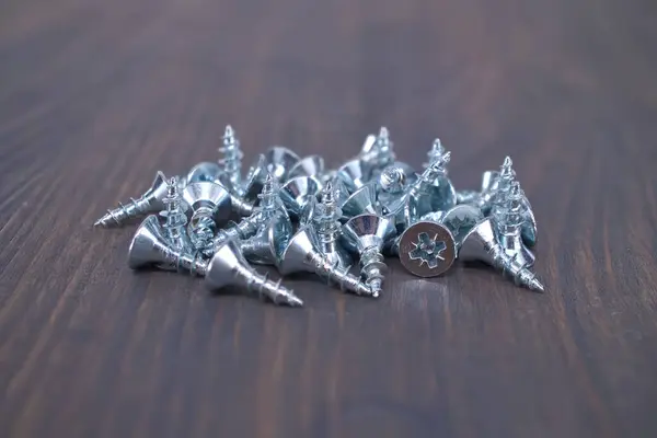 stock image Pile of shiny metal screws on a dark wooden surface, highlighting their star-shaped head design, perfect for construction or DIY projects.