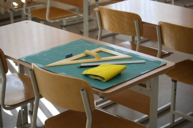 Sınıf masasında cetvel ve kare gibi matematik araçları sergilenirken, bir silgi ve bir kesme paspas üzerindeki temizlik beziyle birlikte.