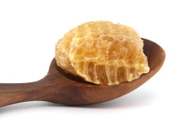 Beyaz arka plana karşı ahşap kaşıkla bal peteği parçasının yakın çekimi doğal tatlılık sergiliyor