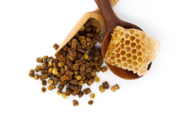 Arı poleni tanecikleri ve bir parça bal peteği beyaz bir zemine karşı ahşap kepçe ve kase üzerinde sunuluyor, doğal sağlık faydalarını vurguluyor..