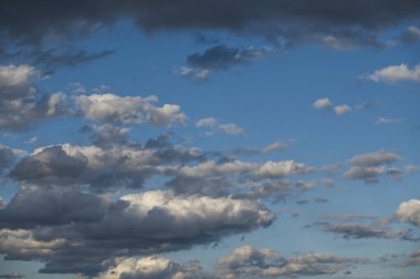 Mavi gökyüzündeki dramatik bulutlar çarpıcı bir zıtlık yaratır, doğanın güzelliğini ve değişen hava modellerini gösterir..