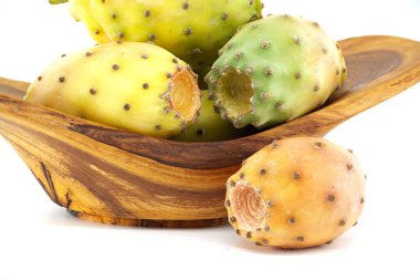 Ahşap bir kasede sergilenen renkli dikenli armut meyveleri, doğal dokularını ve canlı renklerini beyaz bir arka plana vurguluyor.