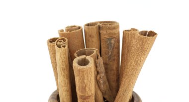 Ahşap bir kasenin içindeki tarçın çubuklarının beyaz bir arka plana yakın plan görüntüsü. Baharat, yemek pişirme ve doğal malzemeler için mükemmel.