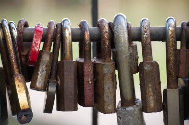 Metal bir çite asılmış yıpranmış asma kilit koleksiyonu güvenlik ve korumayı simgeliyor. Paslanma ve aşınma yaşı ve kullanımı gösteriyor. Endüstriyel ve tarihi bir his yaratıyor.