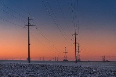 Gün ağarırken sakin bir kış manzarası. Dalgalı elektrik hatları, koyu maviden sıcak turuncuya dönüşen değişken bir gökyüzüne karşı. Zemin hafif buzlu. Huzurlu atmosferi arttırıyor.