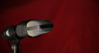 Koyu kırmızı arka planda metal ızgaralı profesyonel stüdyo mikrofonu, müzik kaydı, podcast ve yayın için ideal.