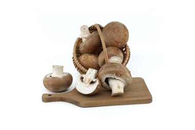 Taze mantarlarla dolu bir hasır sepet, hem bütün hem de dilimlenmiş çeşitleri, zarif bir şekilde ahşap bir kesme tahtasına yerleştirilmiş..