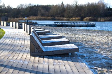 Huzurlu göl manzarası sakin suyu olan kumlu bir sahile bitişik bir sahil boyunca modern ahşap banklar. Rahatlamak ve doğanın huzurunun tadını çıkarmak için mükemmel..