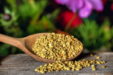 Arı poleniyle dolup taşan tahta kaşığın yakın çekimi, canlı bir çiçek arka planına karşı kurulmuş, doğa ve sağlıklı yaşam tarzı kavramlarını aktarıyor.