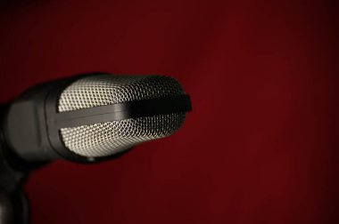 Koyu kırmızı arka planda metal ızgaralı profesyonel stüdyo mikrofonu, müzik kaydı, podcast ve yayın için ideal.