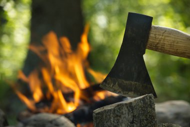 Keskin balta, kamp gezisi sırasında yemyeşil bir ormanla çevrili, çatırdayan bir şenlik ateşinin önünde odunları parçalıyor. Açık hava meraklıları için sıcak ve davetkar bir atmosfer yaratıyor.