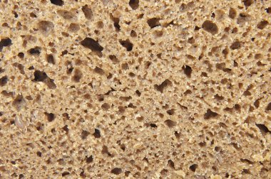 Koyu bir ekmeğin gözenekli dokusunun yakın görüntüsü, hava ceplerini ve yoğun kırıntılarını gösteriyor.