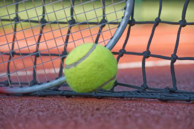 Tennis ball and racket are lying on the net of a clay court, suggesting a recent match and evoking the spirit of competition and sportsmanship clipart