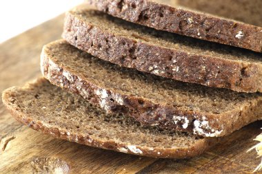 Dilimlenmiş siyah ekmek ahşap bir tahtanın üzerinde oturur, yoğun dokusunu ve zengin kahverengi rengini sergiler. Görüntü, pişirme, yemek ve dokuları resmetmek için mükemmel..