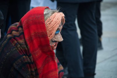Geleneksel maskeli ve şallı bir sanatçı kültür festivali veya tiyatro performansına hazır olup, gizem unsuru ekliyor.