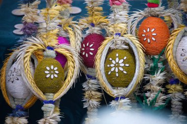 Örülmüş buğday ve çiçek desenleriyle süslenmiş el yapımı Paskalya yumurtalarının yakın çekimi, canlı renkler ve karmaşık detaylar.