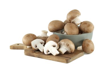 Taze kremini mantarlar, bütün ve dilimlenmiş, seramik bir kaseden taşan mantarlarla ahşap bir kesme tahtasının üzerinde sunuluyor..