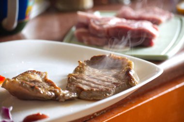 Bir tabak pişmiş biftek, hafif buharda pişmiş, servis edilmeye hazır. Çiğ et kesme tahtasının arkasında oturur ve lezzetli bir yemek hazırlar..