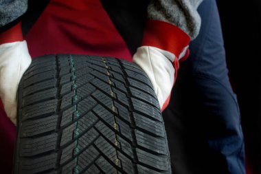 Tamircinin eldivenli elleri lastiği inceliyor, lastik izlerini ve otomotiv bakımını vurguluyor. Profesyonel bir atölye içerisindeki araç bakımında güvenlik ve hassasiyeti gösterir