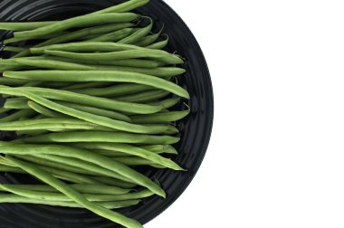 Taze ve canlı yeşil fasulyeler siyah bir tabakta güzelce sıralanmış, görsel olarak çekici bir kontrastlık yaratıyor ve sağlıklı ve lezzetli bir yemek hazırlığı öneriyor.