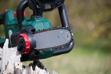 Yakın plan görüntü, bulanık bir arkaplana karşı zincir, çubuk ve ergonomik tasarım elementlerini vurgulayan, pille çalışan modern bir testere içerir..