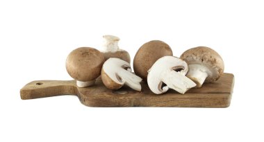 Bazı cremini mantarlar, bazıları bütün ve bazıları dilimlenmiş, beyaz arka planda küçük, kırsal bir ahşap kesme tahtasında sunuluyor..