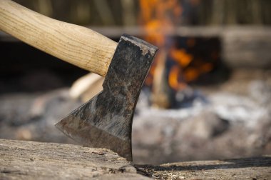 Baltayı ahşap bir blokta sıkışmış, arka planda yanan bulanık bir ateş kırsal bir alanda. Kamp yapmayı, odun kesmeyi temsil ediyor..