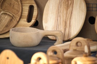 Rustik ahşap mutfak gereçleri ustalıkla dizilmiş, aralarında bir kuksa bardağı, tabak ve tahtalar, doğal ahşap tahıl ve işçilik sergileniyor..