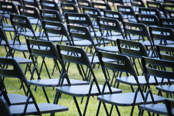 Bir çimenlikteki sıra sıra dizilmiş siyah katlanır sandalyelerin düzenlenmesi, açık hava ortamında etkinlikler veya toplantılar için uygun düzgün, tek bir desen oluşturur..