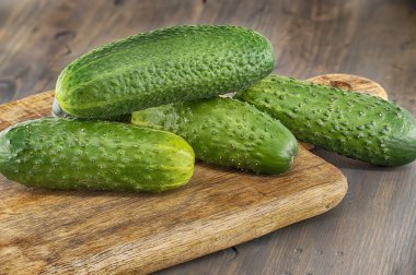 İnişli çıkışlı derili taze salatalıklar ahşap kesim tahtasının üzerinde dinleniyor sağlıklı yemek ve organik ürünleri ön plana çıkaran canlı ve kırsal bir mutfak sahnesi yaratıyor.