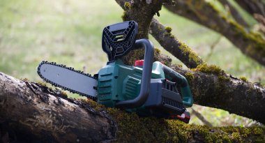 Yosun tutmuş bir ağaç dalında duran elektrikli testerenin detaylı bir görüntüsü. Odun kesmek için güçlü bir araçtır ve çeşitli projeler için kullanılır..