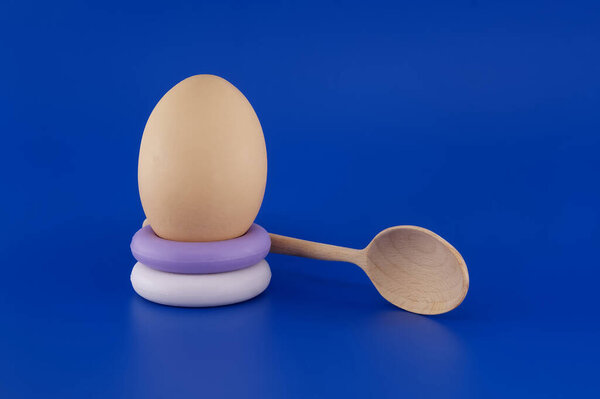 Коричневое яйцо лежит на стопке мыльных колец, дополненной деревянной ложкой на ярком синем фоне.