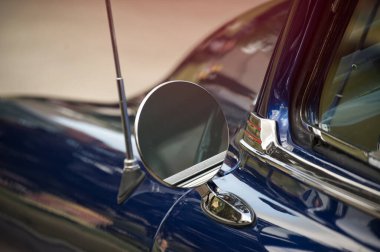 Eski bir arabanın yan aynasının detaylı görüntüsü, parlak mavi boya ve nostaljik tasarım sergileniyor..