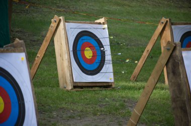 Okçuluk hedefleri rengarenk boğa güreşlerine gömülü, çimlerle çevrili açık bir ortama kurulmuş, rekabetçi ve eğlenceli bir okçuluk oturumu sırasında hassasiyet ve odaklanma gösteriyorlar..
