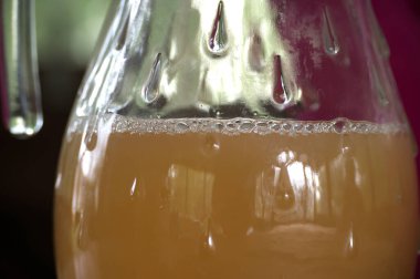 Bir cam içecek kabının yakın çekimi, sıvının etrafındaki yoğunluğu ve kabarcıkları gösteriyor, canlandırıcı ve davetkar bir görsel sunuyor..