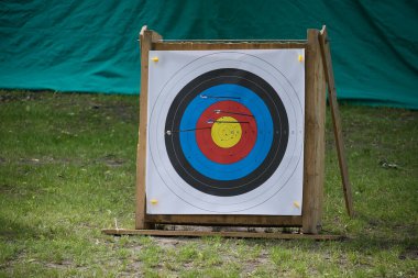Okçuluk açık havada hedefleniyor. Hedefleri hedef alan ve çevreleyen bölgelere isabet eden oklar görülüyor..