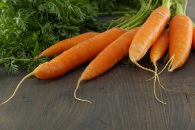 Toplanan organik havuçlar ve yeşil tepeler kırsal bir ahşap yüzey üzerinde doğal ürünler sergiliyor..