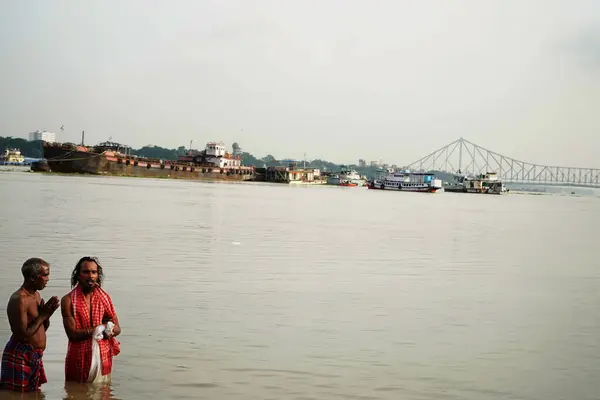 stock image Two person are praying for god in ganga ghat of Kolkata showing Howrah bridge in Bakcground during mahalaya Tarpan