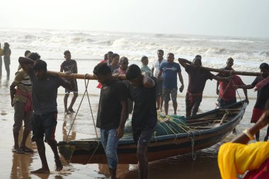 06 Ağustos 2023, Puri, Odisha, Hindistan. Çalışkan balıkçılar balıkçı teknelerini denizden sahile taşıyorlar.