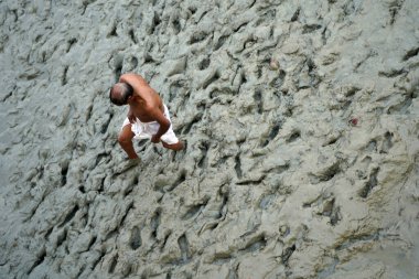 14 Ekim 2023, Babughat, Kolkata, Batı Bengal, Hindistan. Çamurlu arazide yalın ayak yürüyen yaşlı adam.