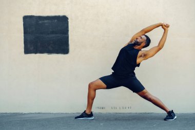 Çömelme bacağı ve kollarını esneten bir adam.