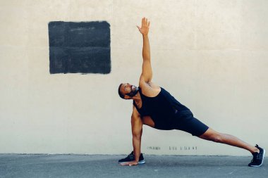 Spor kıyafetleri giyen formda bir sporcu, iyileşme ve canlılık için güçlerini, dengelerini ve esnekliklerini artırmak amacıyla iç mekanda egzersiz yapıyor..