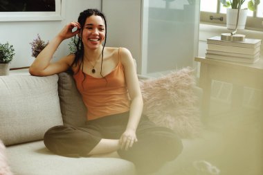 Genç melez kadın evdeki kanepede oturuyor.
