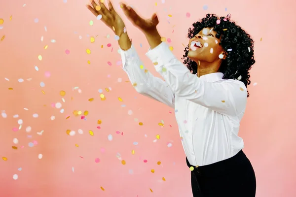 Stock image A special occasion - Portrait of a happy woman with arms out, smiling at confetti falling. Studio shot over pink background