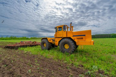 Bahar fotoğrafçılığı, ziraat makineleriyle manzara, bir traktör tarlayı sürüyor, tarlayı sürüyor, kuşlar ekilebilir arazinin üzerinde uçuyor.