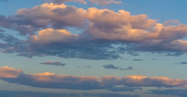 Batan güneşin sıcacık parıltısıyla yıkanan bulutların nefes kesici görüntüsü. Tabiat tuvalinin dingin güzelliği ve sükuneti. Huzur ve merak uyandıran hayranlık uyandıran bir bakış açısı.