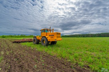 Bahar fotoğrafçılığı, ziraat makineleriyle manzara, bir traktör tarlayı sürüyor, tarlayı sürüyor, kuşlar ekilebilir arazinin üzerinde uçuyor.